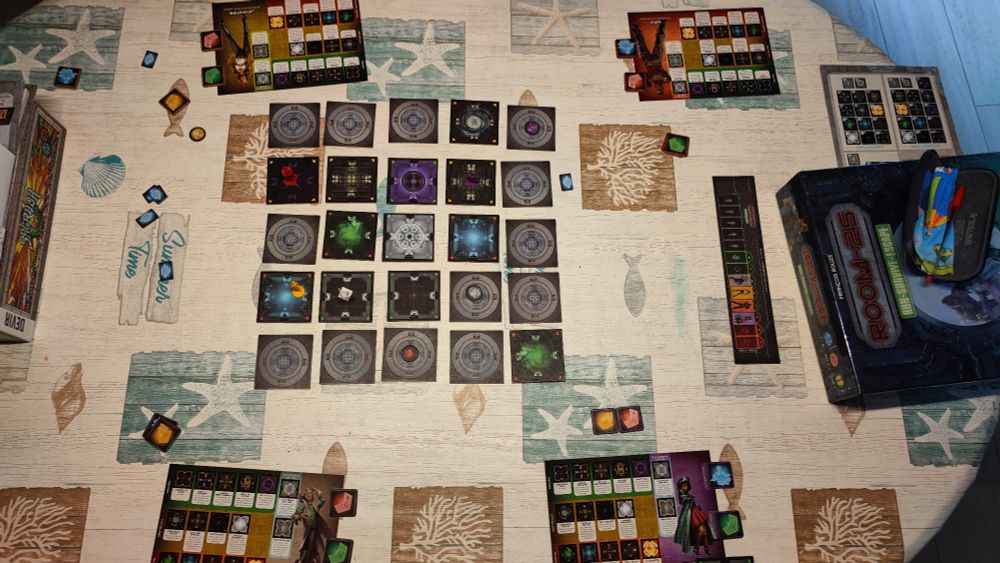 Taula amb el joc a mig jugar, mostra un taulell central composat de 25 fitxes quadrades representant habitacions, algunes estan cara amunt mostrant el contingut de l'habitació, altres cara avall. Sobre algunes de les fitxes hi ha els peons q representen cada jugador, cadascun d'un color diferent. Cada jugador, a més, té un cartró amb la descripció del seu personatge, l'efecte de cada tipus d'habitació i les accions q farà aquell personatge aquell torn. A la dreta hi ha una tira de cartró addicional indicant l'ordre en q juga cada jugador així com els torns restants per acabar el joc.