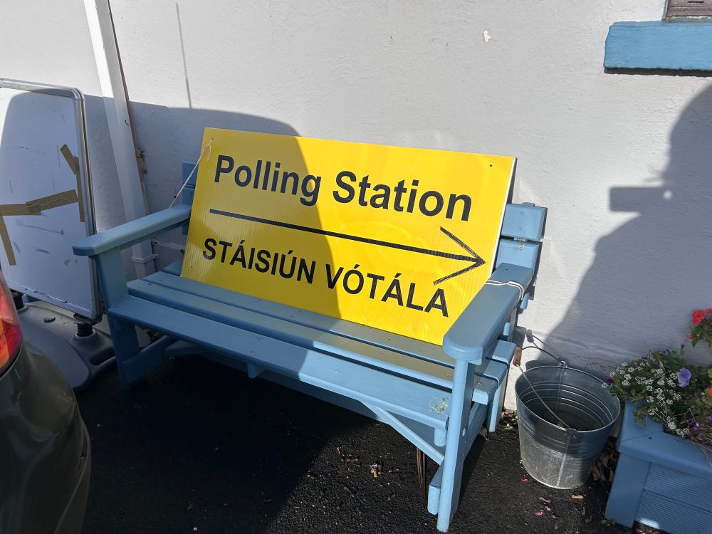 A polling station / Stáisiún vótála sign on a blue bench outside 