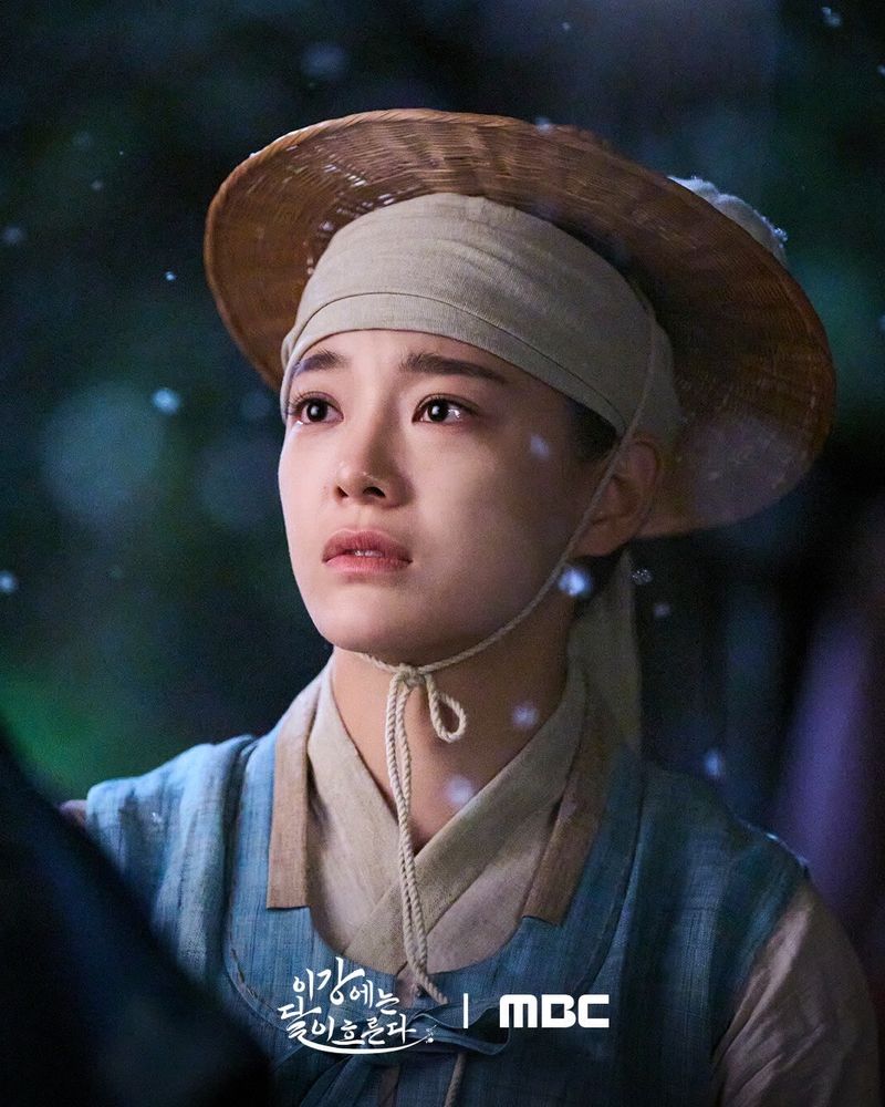 韓国ドラマ「この川には月が流れる」のスチール写真。
韓服(庶民の男性用)と笠を身に着けた若い女性(キムセジョン)が、雪の降る夜に涙ぐんだ表情で見上げている。左下にタイトル「인간에는 딱 인흠로다」および放送局「MBC」の文字。