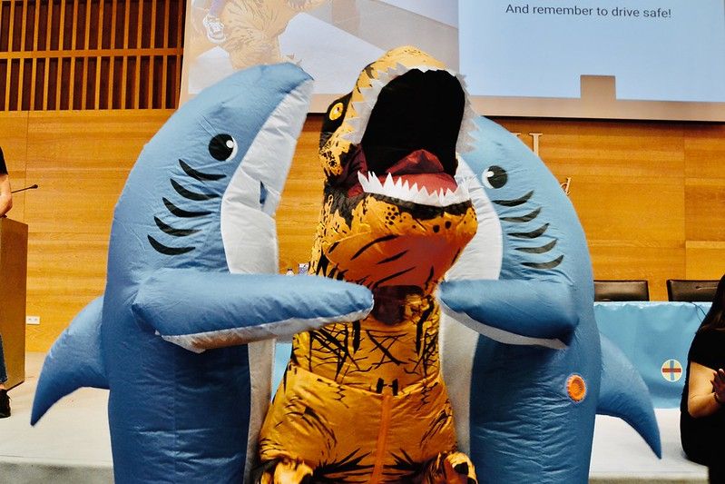 Foto del cierre de Commit donde las "mascotas" de esta edición, un T-Rex y dos tiburones, se abrazan en el escenario del auditorio.