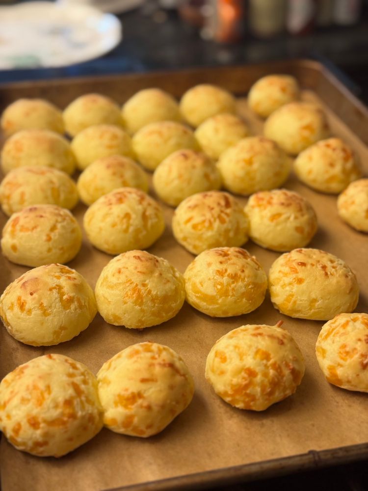A tray of Brazilian Cheese Breads, baked as one-inch rounds, just baked and resting on parchment paper. 