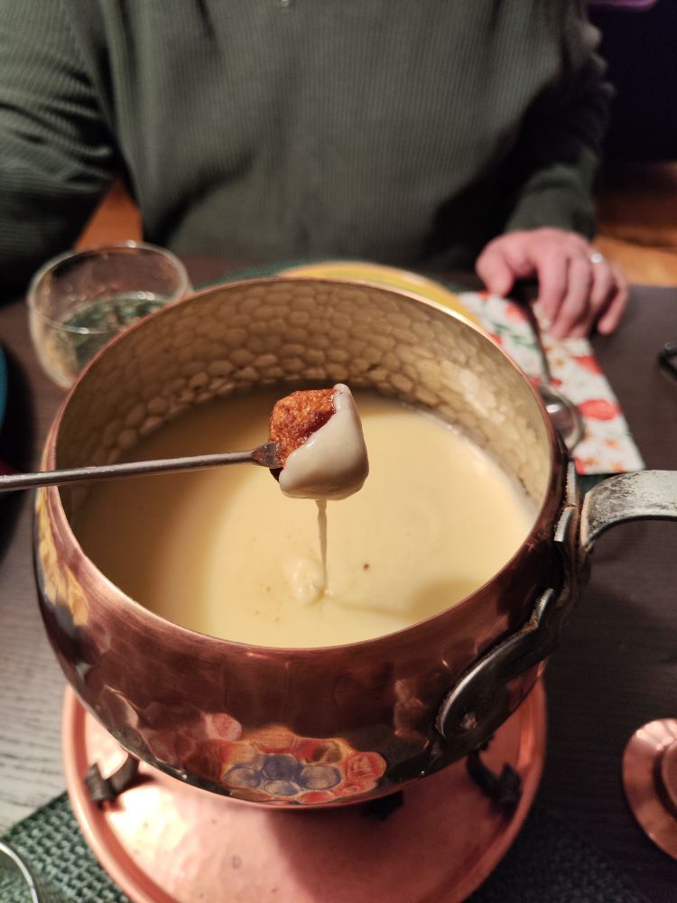 A vintage copper fondue pot, half full of cheese fondue, with a meatball on a fork above it, slowly dripping cheese back into the pot. 