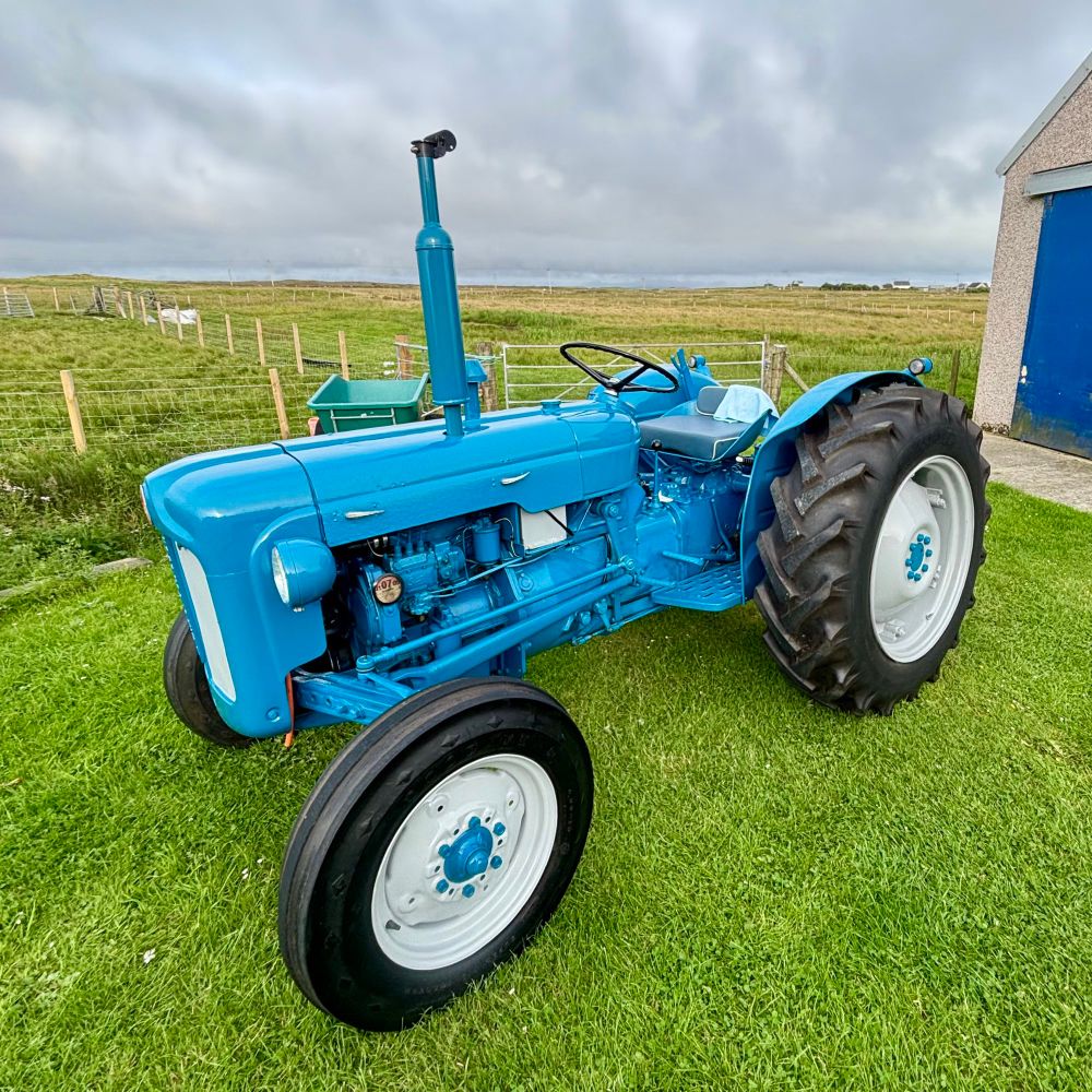 A Fordson Dexta tractor outside a shed renovated and painted with empire blue paint