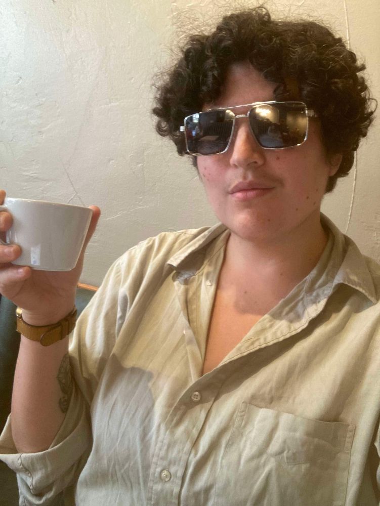 Molly as Agent Blanc drinks coffee and wears sunglasses.