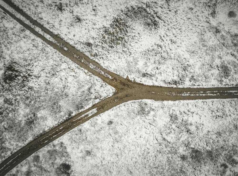 An overhead photograph of a road passing through snowy fields. The road forks toward the left of the picture.