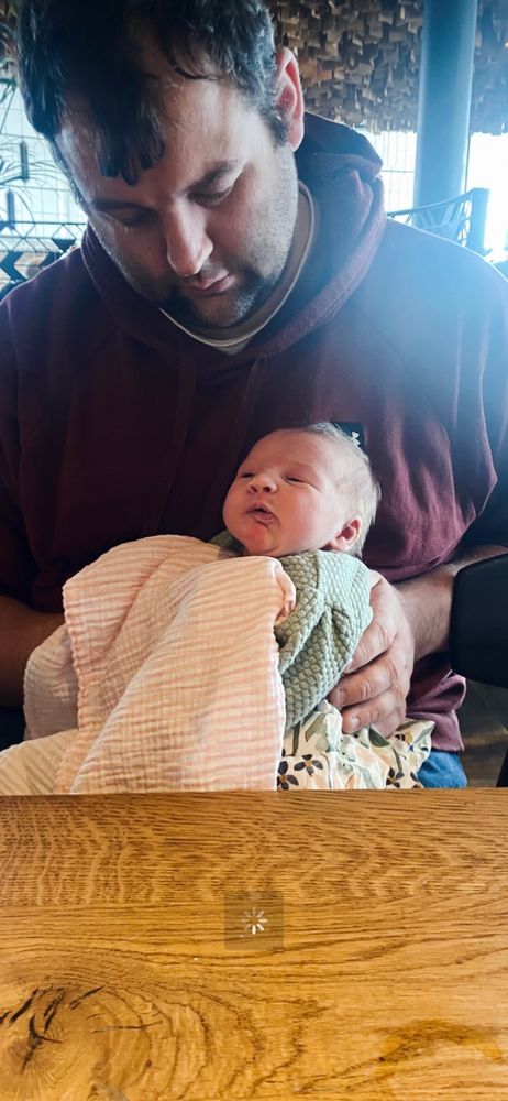 A little baby being burped on her dad’s lap.
