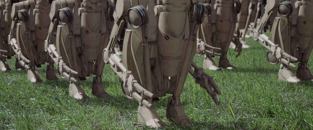 A screencap from Star Wars Episode I: The Phantom Menace, showing a closeup shot where half a dozen Battle Droids are crouching in grass.