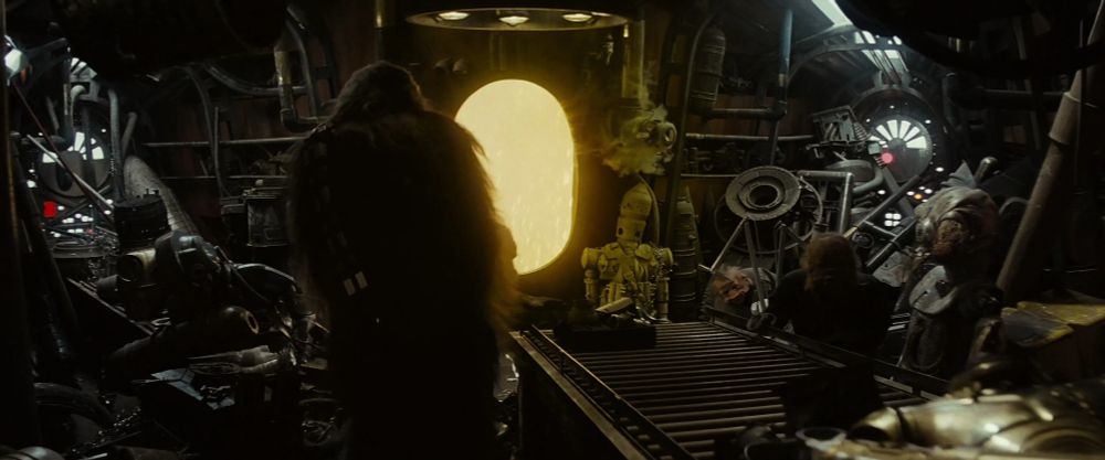 A screencap from Star Wars: The Empire Strikes Back, where Chewbacca is in a room full of droid junk. On the left in the shadows is a prop made with some TIE Pilot helmet parts.