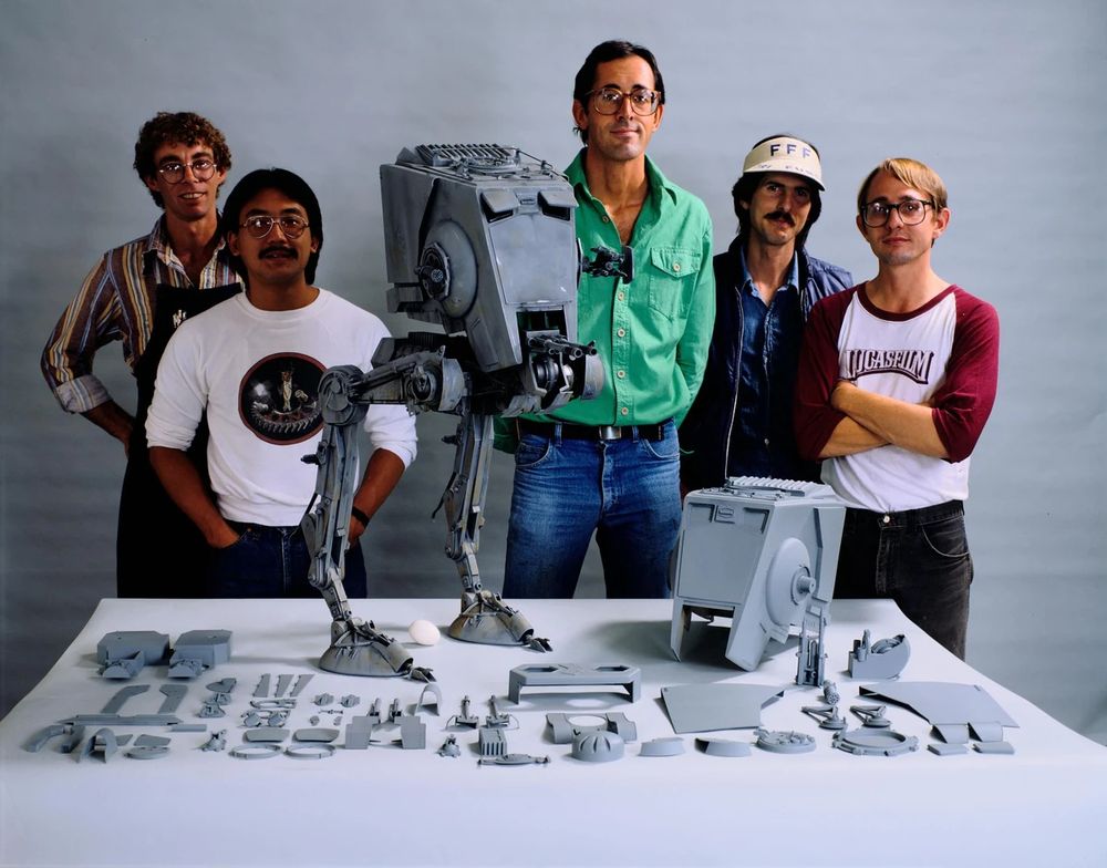 Members of the ILM crew standing behind a table with a large, fully painted AT-ST pyro model and also unpainted cast components for another.