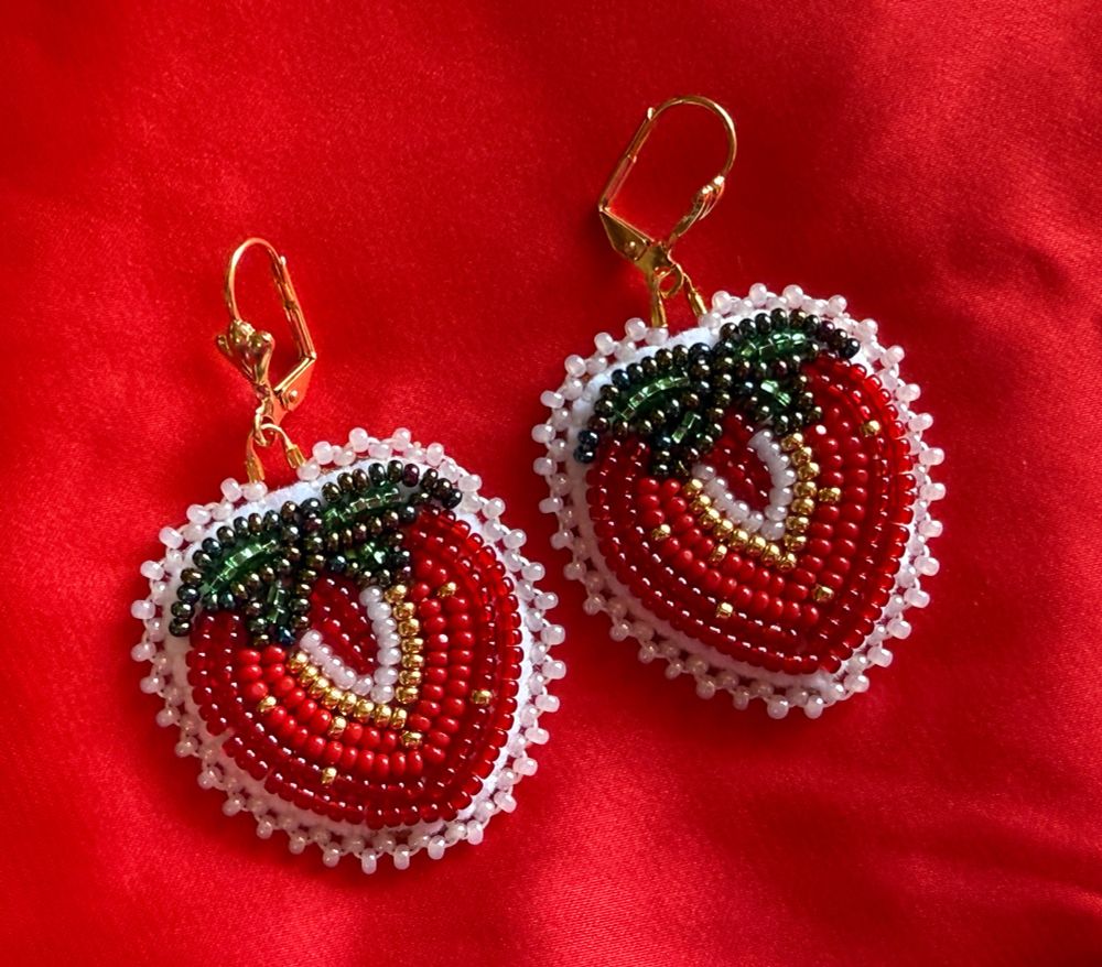 Beaded red strawberry earrings. Flat stitch design. Gold plated lever hooks. Laying on red satin.

