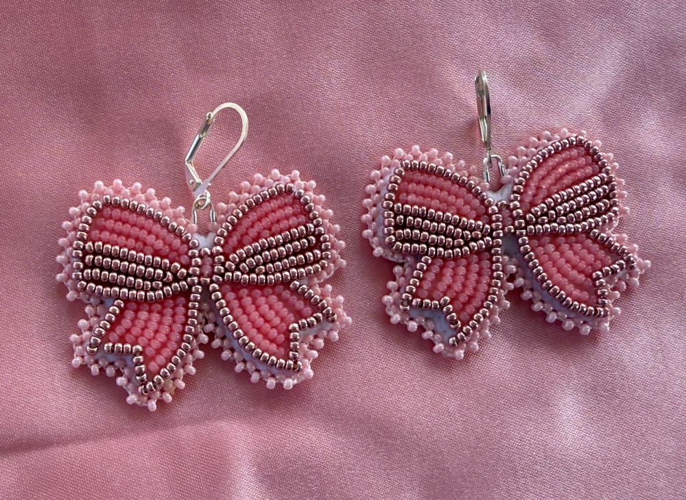 Beaded earrings in the shape of pink bows. Flat stitch design. Laying on pink satin.