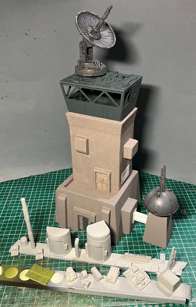 A tall, grey tower with a darker grey top and satellite dish on that with some lighter grey bits and bobs in the front. All in front of a grey background. Can you sense a theme…

There’s a little grey tower off to the right with a dark grey shield generator on it. 

In fact, the only things that aren’t grey are the cutting mat it’s sat in and the front door, which is green. 