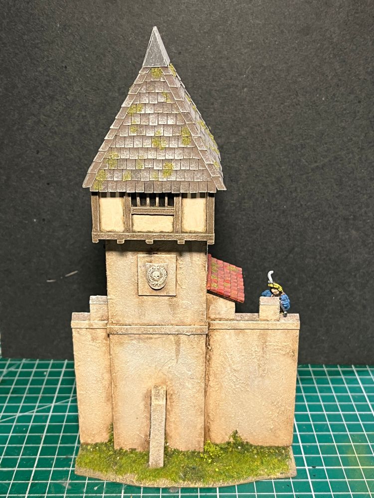 One of the completed town wall sections. Beige in colour, this one has a small tower in the middle as well as a tiled roof. The top of the tower is half timbered and there is a shield motif just below that. Our handgunner has had his ale and is now back on the wall on lookout. 