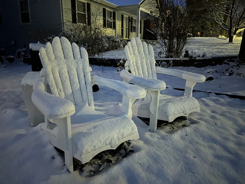 A pair of snow-covered Adirondack chairs