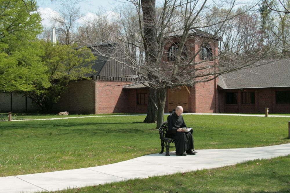 a monk sitting on a bench reading at St. Gregory's Abbey, a Benedictine monastery in the Episcopal Church near Three Rivers, Michigan USA