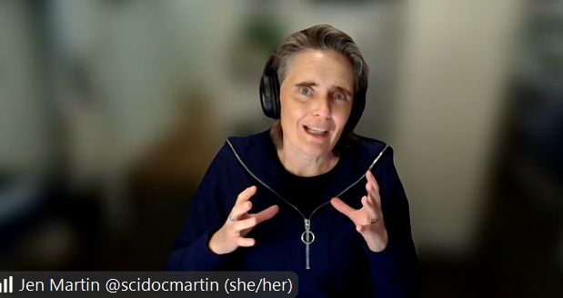 Jen Martin, wearing headphones and a black zip-up jacket, presenting her seminar about communicating research. 