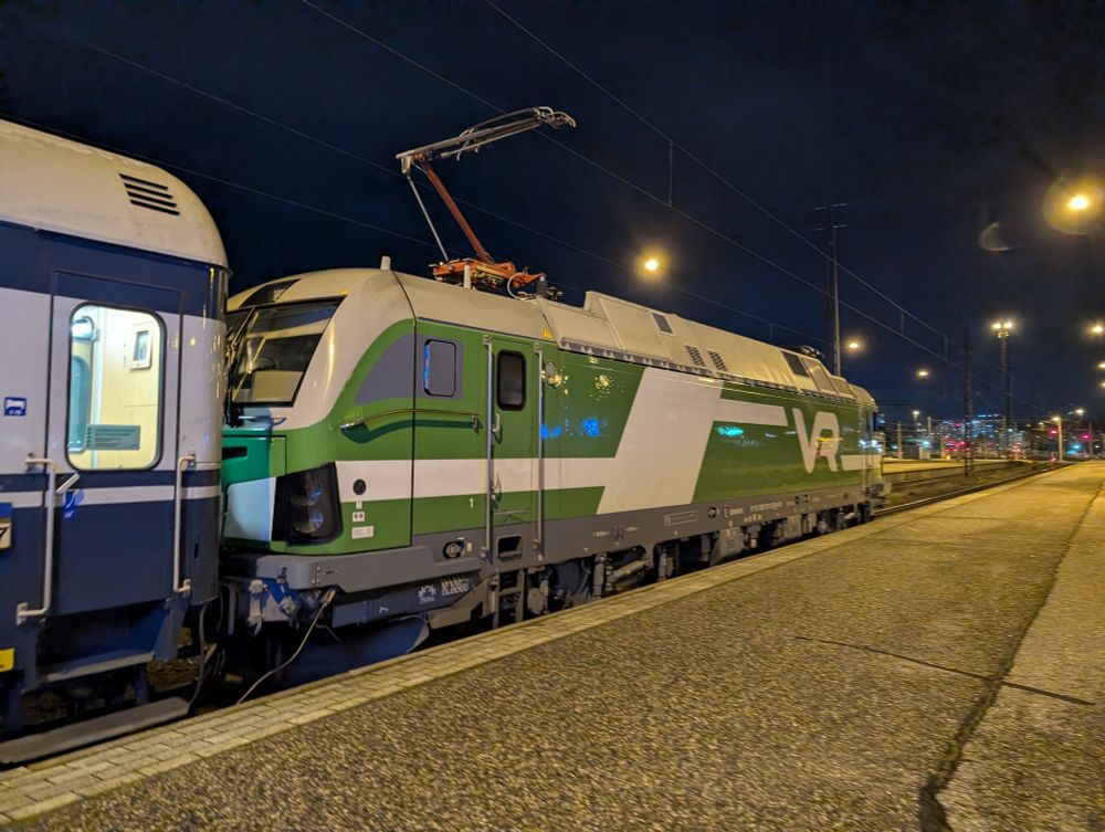 Photo of a green VR locomotive at the country-end of track 8 at Helsinki station. Attached to the rear of it but mostly out of view is an old white and blue VR sleeper carriage.
