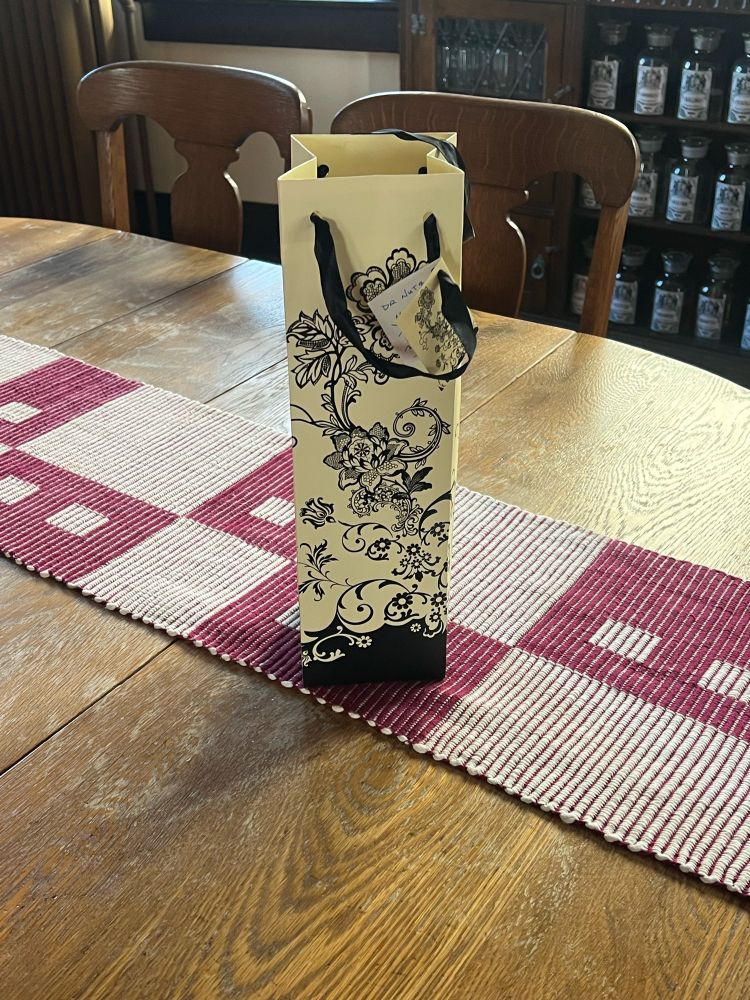 Black and cream wine gift bag on a dining room table with a maroon and white table runner 