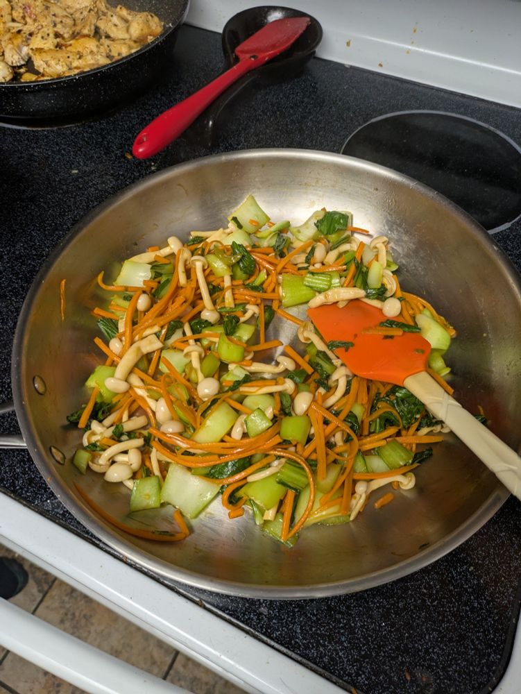 A pan with julienned carrots, cabbages, mushrooms, and garlic.