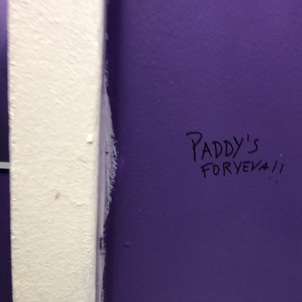 Handwritten in a black marker on a purple-colored wall are the words Paddy's FORYEVA!!