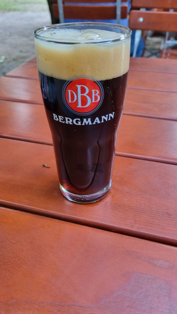 Ein Glas, gefüllt mit Adambier der Bergmann Brauerei. Das Glas steht auf einem braunen Lattentisch.