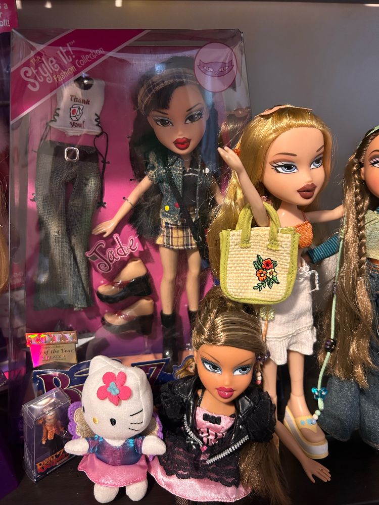 Collection of Bratz dolls sitting on shelf.