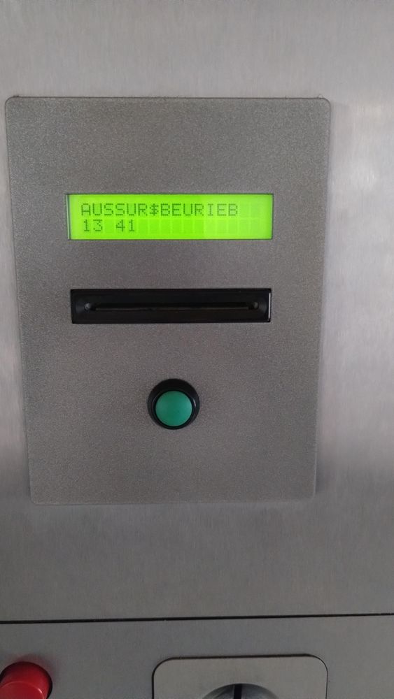 Ein Kartenleser. Oben ein beleuchtetes Display, auf dem "AUSSUR$BEURIEB" und "13:41" steht, darunter der Schlitz für die Karte, darunter ein grüner Knopf.