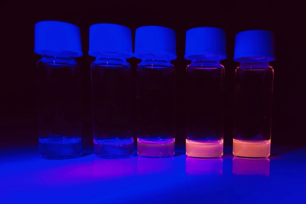 Photograph of luminescent nanocrystals in vials with a blacklight behind them. The emission becomes brighter and oranger from left to right. 