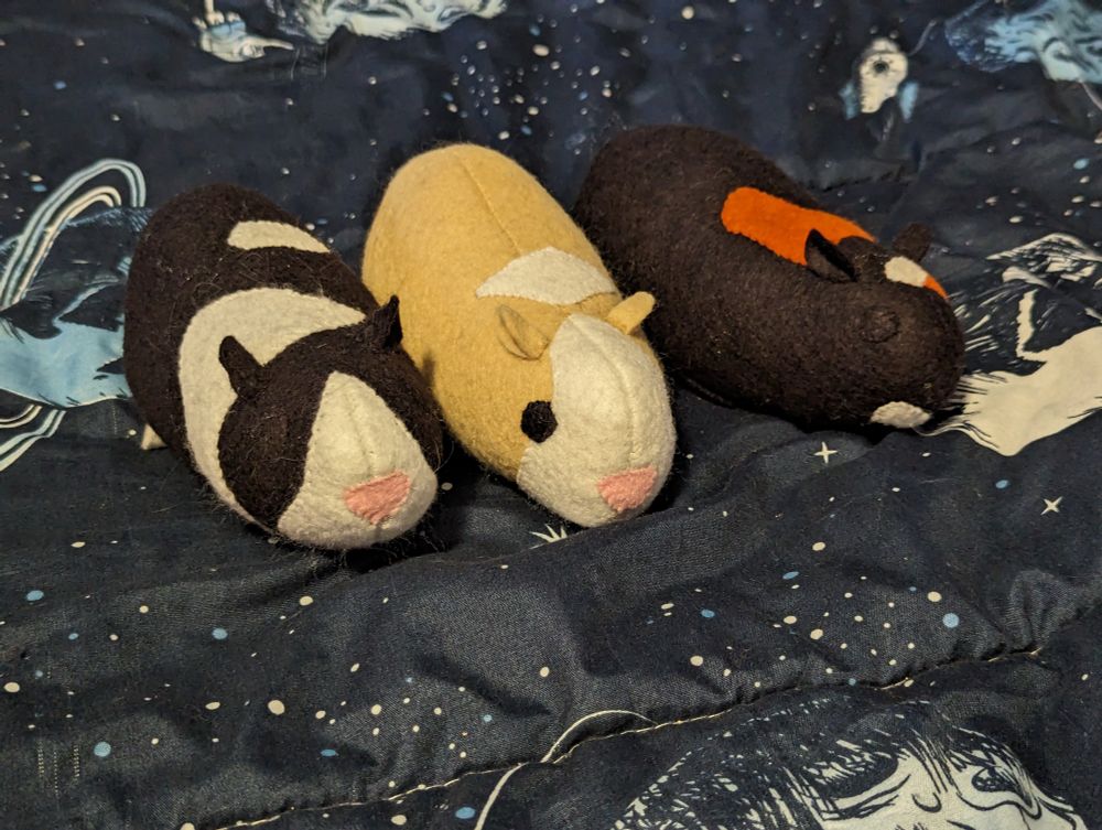 A photo of three plush guinea pigs. They're shaped like potatoes with little ears and faces