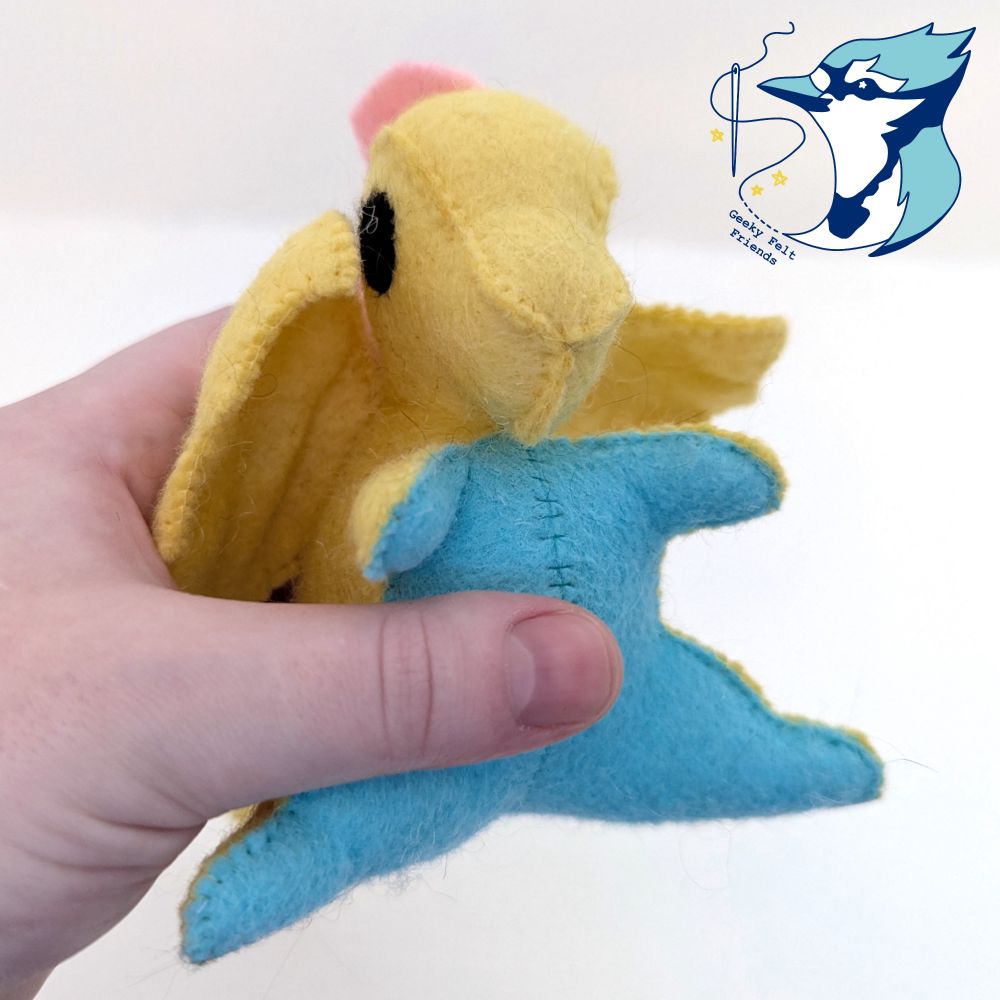 A closer photo of a pale yellow, ocean blue, and pale pink baby dragon plush