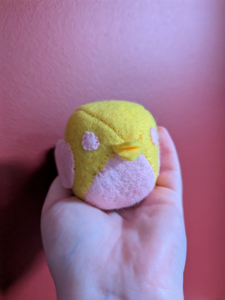 A photo of a small plush bird that fits in the palm of a hand. It is very round, basically a ball, with small wings and beak. 