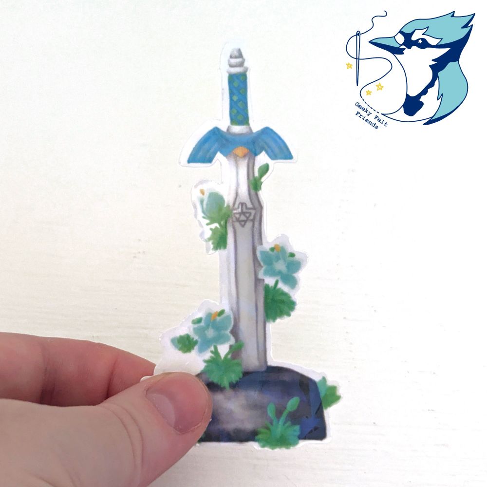A sticker of the master sword, which is a broadsword with a blue wing shaped guard. It is stood in a stone pedestal, with blue lilies growing around it. It has a gold gem imbedded in the hilt, and a triangle design a third of the way down the blade. The sticker has a holographic shards effect.