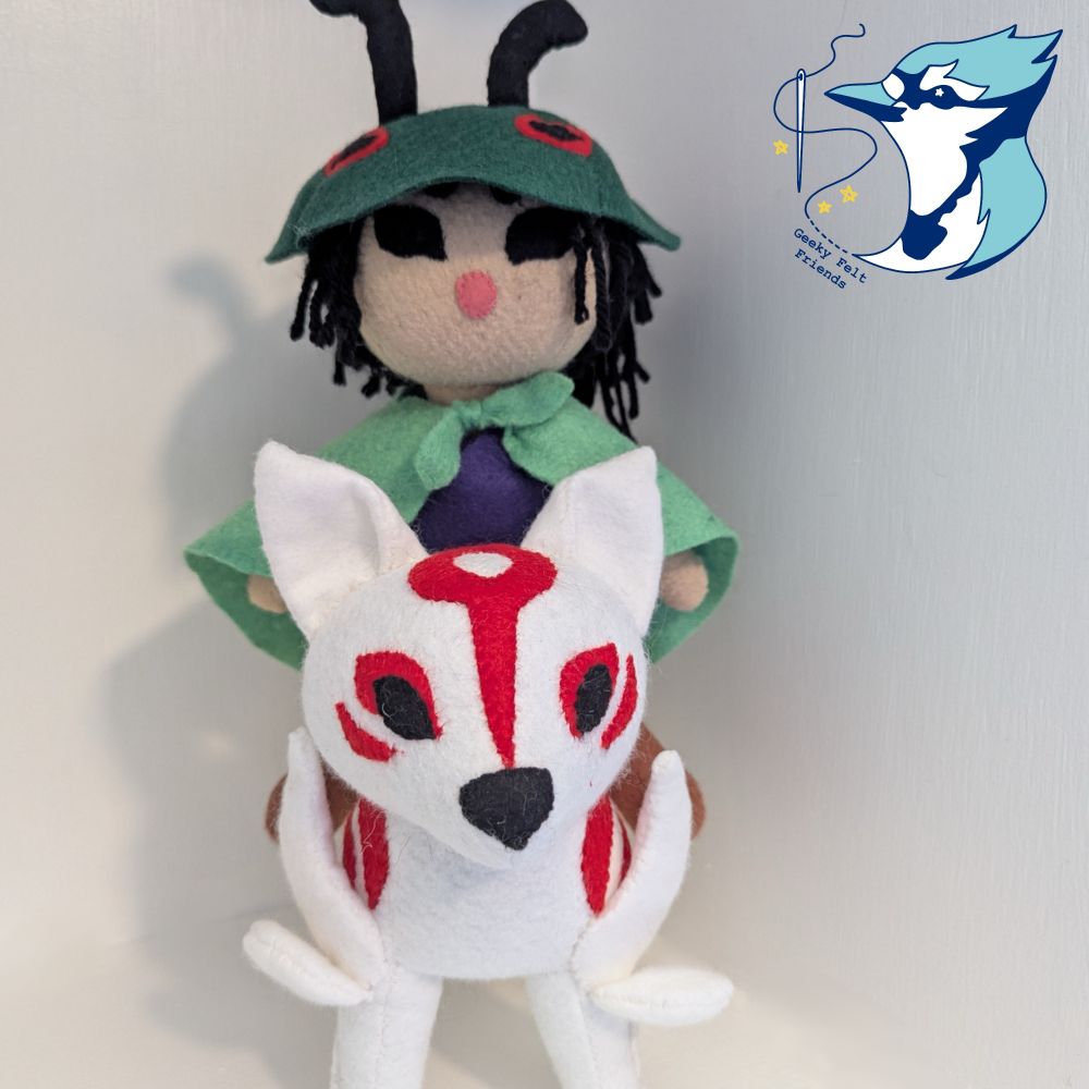 A photo of a plush white wolf with red markings, a doll on her back who wears a green cloak and a beetle shell hat.