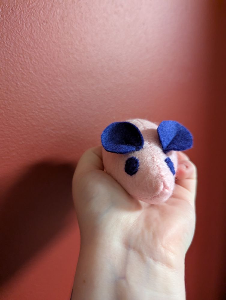A photo of a small plush mouse that fits in the palm of a hand. It has a teardrop shaped body that ends in a pointed nose, and big round ears.