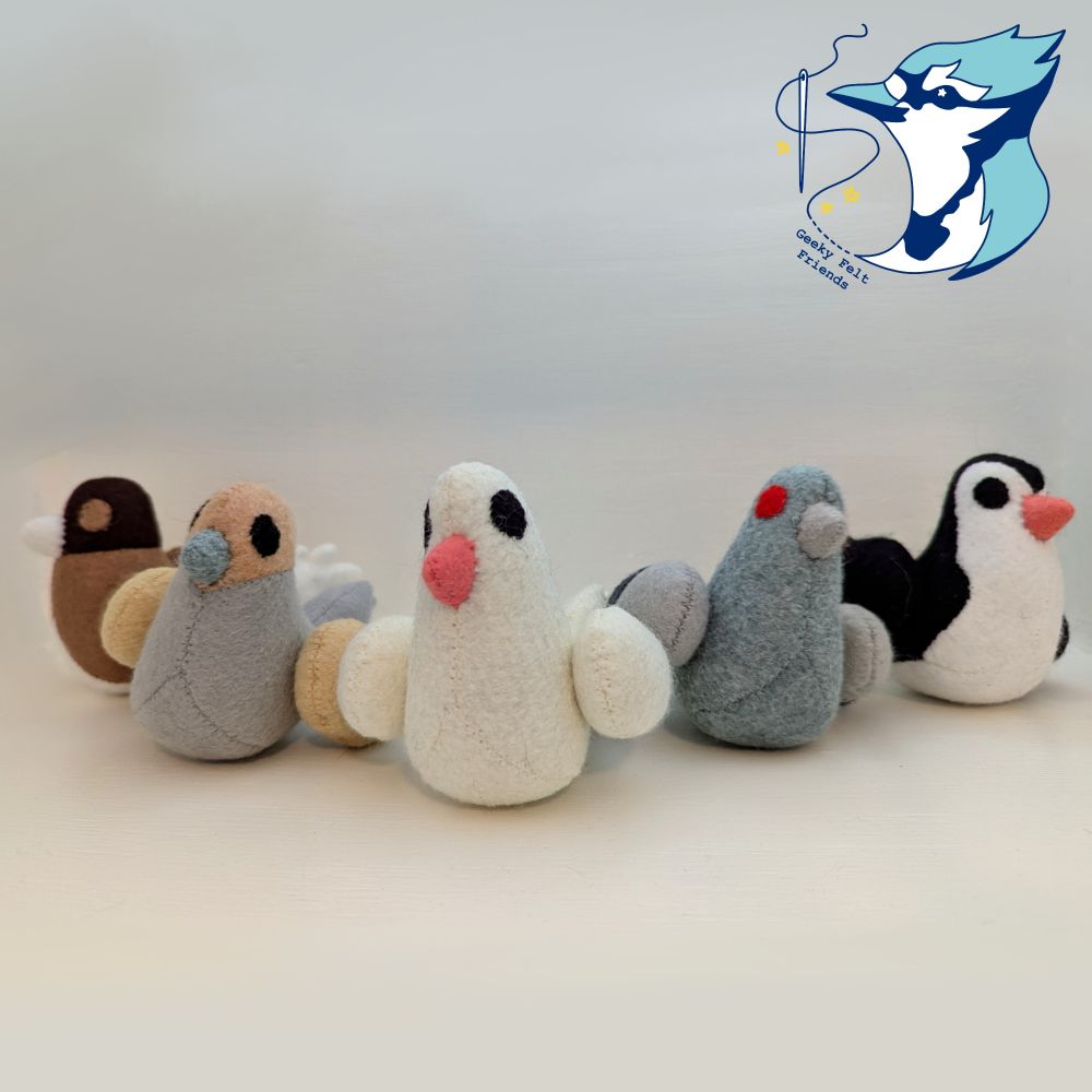 A photo of five plush pigeons, cute and chunky. A brown one, a mourning dove, a white one, a gray one, and a black and white one.