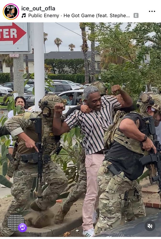 Two men in fatigues with machine guns grabbing the shoulder and arms of a Black man in civilian clothing. Another man in fatigue with a machine gun is in the foreground of the man being restrained. 