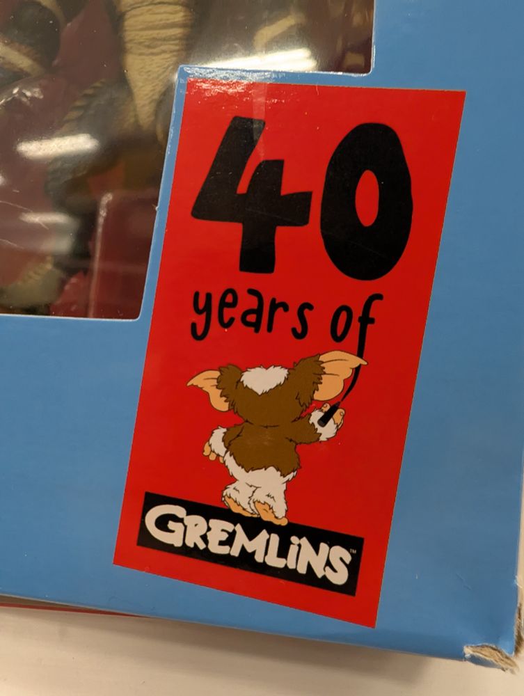 a "fun" label on a Gremlins action doll box, it's a red box featuring Gizmo, the lame bland mogwai from where all the cooler gremlins come from, facing away as he "paints" the words '40 years of Gremlins' -- this is a terrorism. no damn way it's been 40 years since Gremlins. wth Gizmo. caca. 