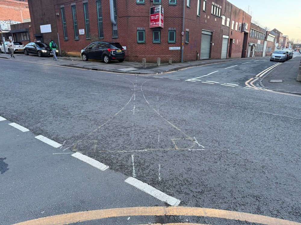 A crossroads with chalk markings to show where bollards will go to prevent through-traffic as traffic will only be able to turn left.