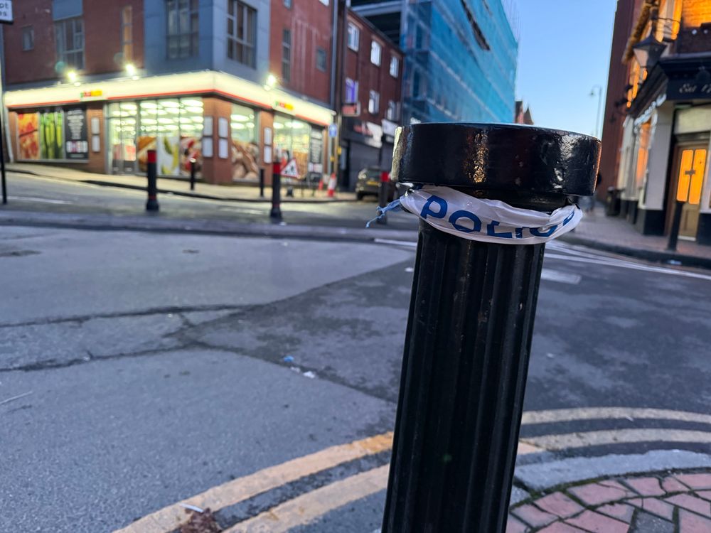 In the foreground is a bollard with the remainders of police tape. In the background is a new set of bollards to stop motor traffic making certain turns.