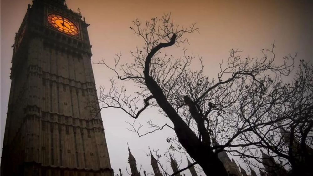 Big Ben rises into a dim, moody sky, framed by leafless, gnarled tree branches, creating a dramatic, Halloween-inspired London cityscape.