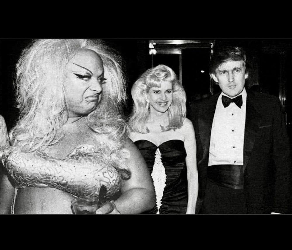Divine looks back over her shoulder at Donald and Ivana Trump. Divine looks disgusted by what she sees. Black and white photo. 