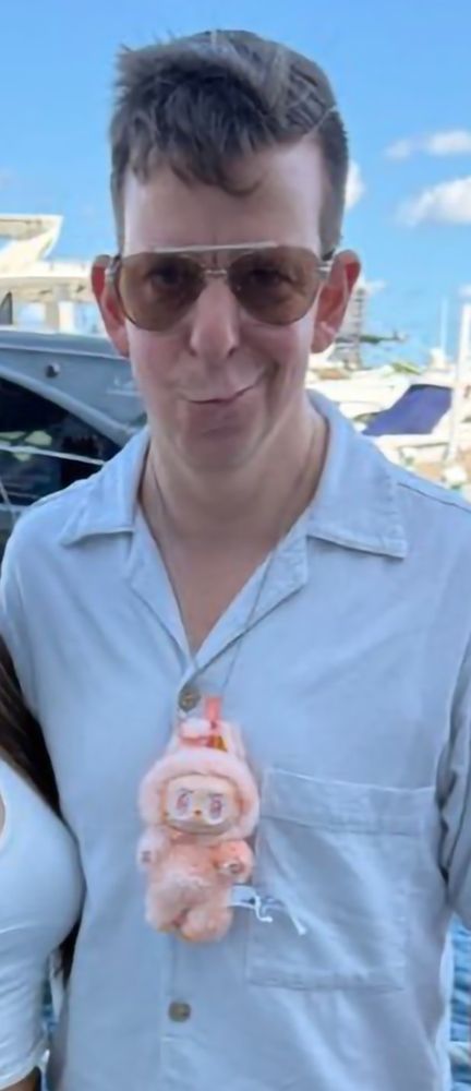 Some cartoonish looking dipshit, maybe like a dork NPC in Grand Theft Auto, who has a small animal doll on a necklace. Apparently this doll is known as a Labubu.