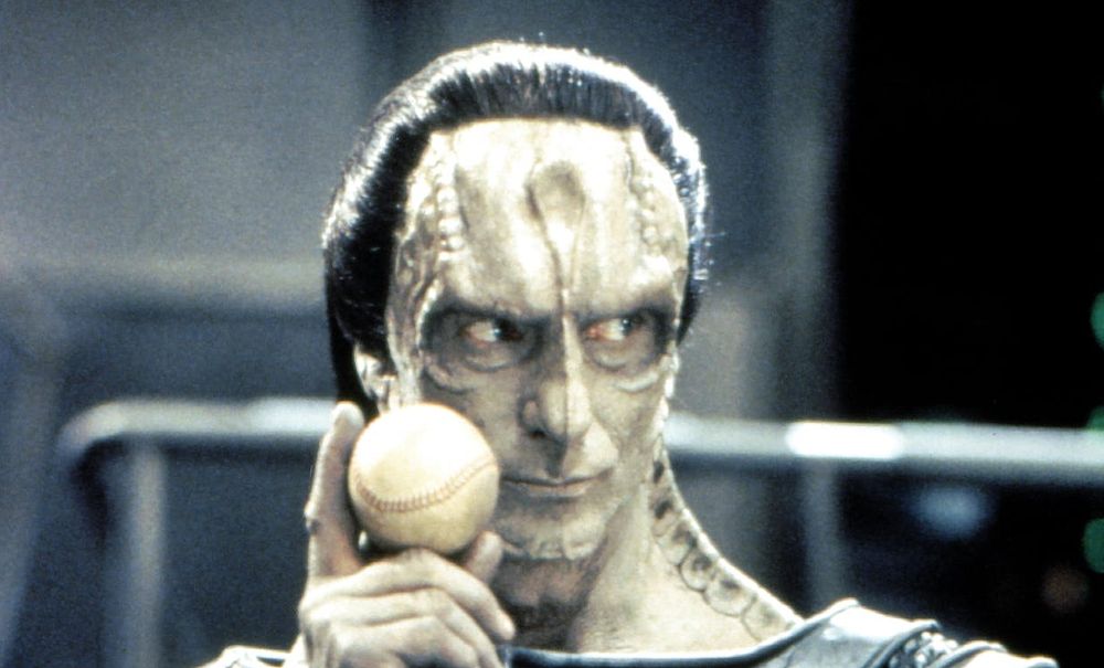 Gul Dukat, a Cardassian (an alien with large ridges on his forehead and neck) holds up a baseball while looking judgemental 