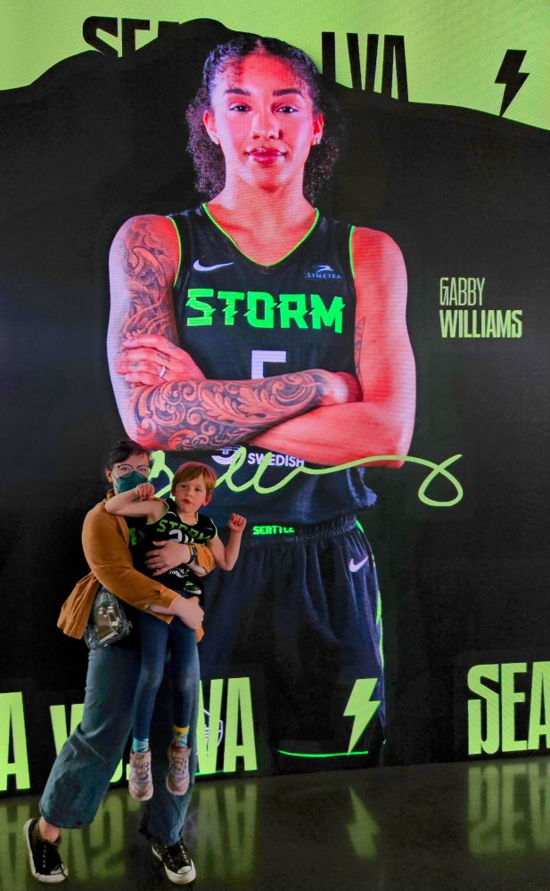 Me, white woman with a 5 y old in my arms. We are posing in front of a screen featuring Gabby Williams of the storm. 