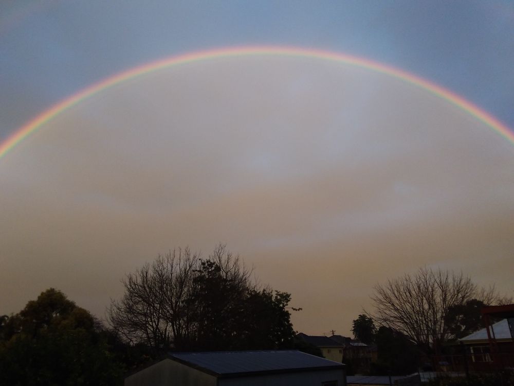 Photo of double rainbow, where the sky beneath the arc of the main rainbow is a lighter colour than the sky above the arc.