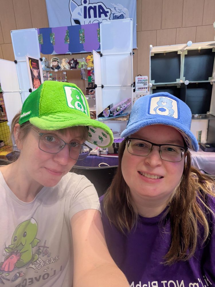 Two girls with carebear basecaps, one in green, one in blue, both are wearing glasses