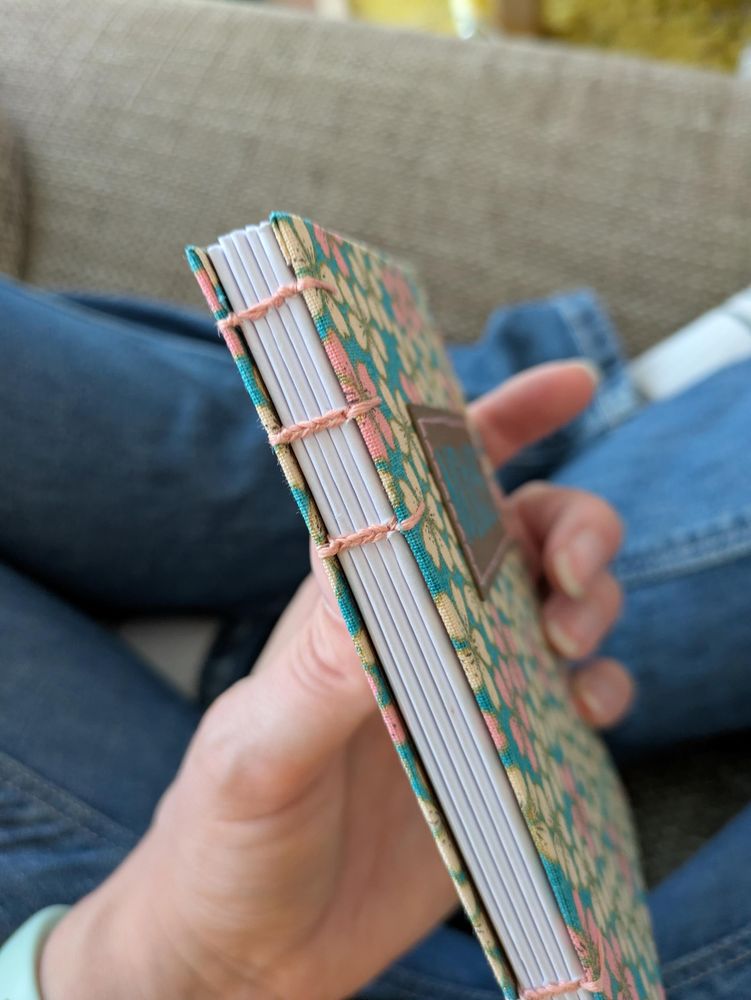Hand holding a self bound book, showing the back. It's bound with light pink thread.