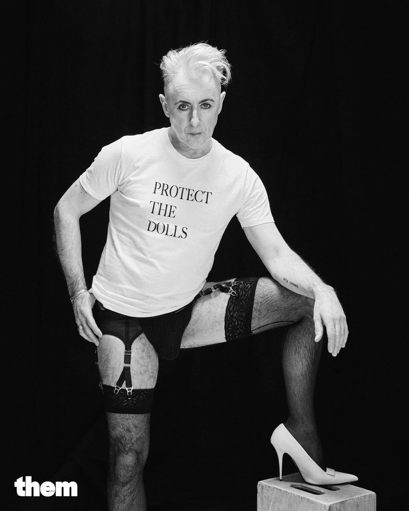 alan cumming in a protect the dolls tshirt, garters, stockings, and heels