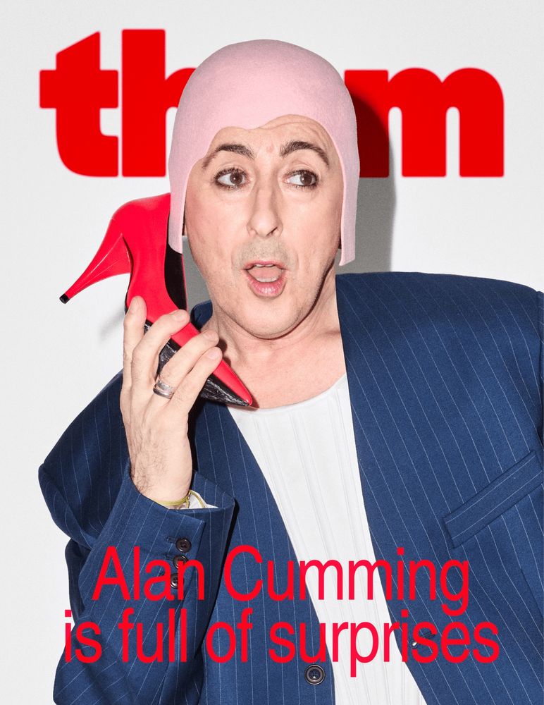 alan cumming wearing a felt hat, a blue blazer and a tank. he’s holding a red stilletto to his ear as though it’s a phone. the them logo is at the top of the image, and the coverline is “alan cumming is full of surprises”