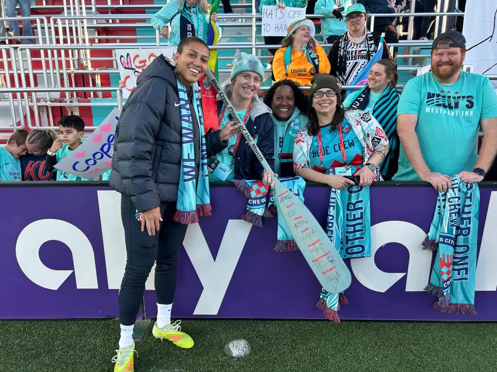 Picture of Bia holding the Player of the Month oar while wearing her Blue Crew scarf standing with members of the Blue Crew board 